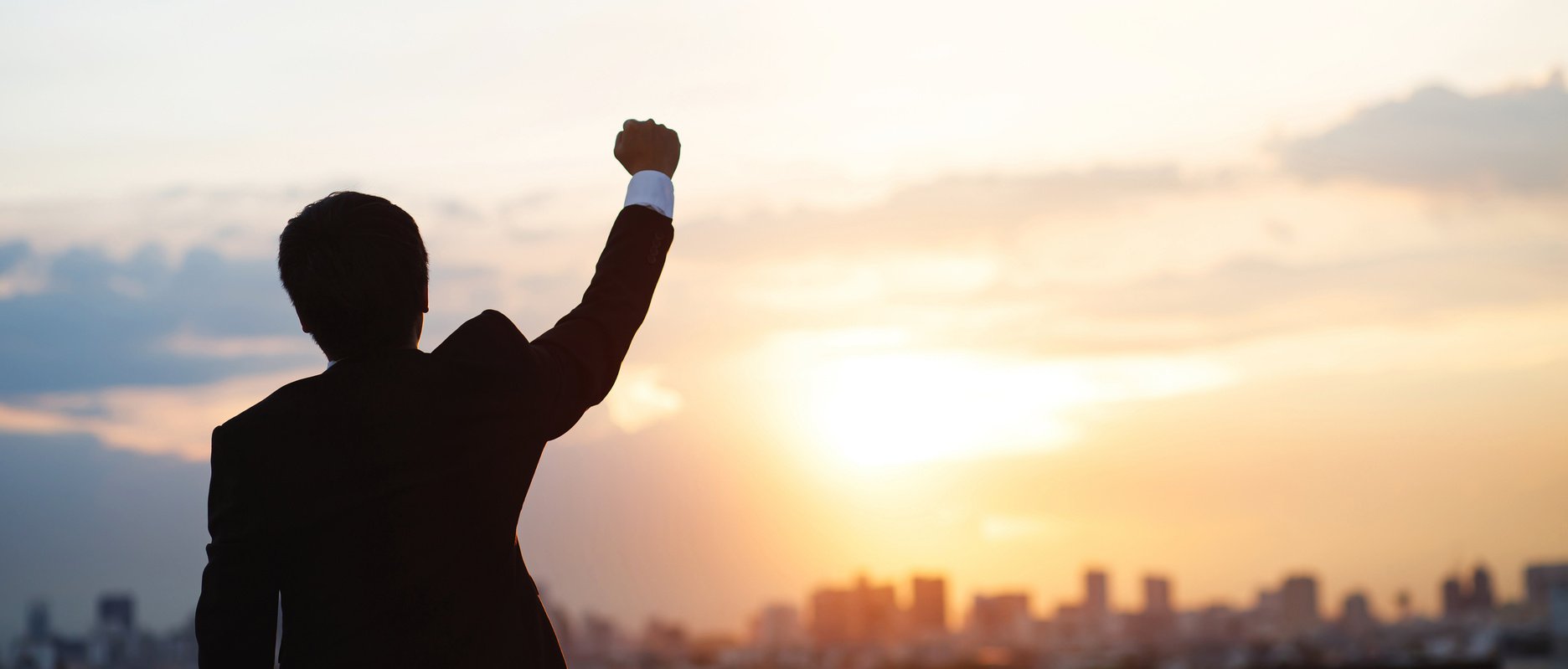 Businessman Raising Hand in the Sky at Sunset